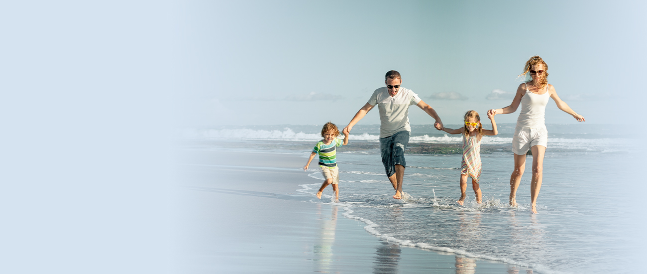 Family holding hands and walking along the beach shore.